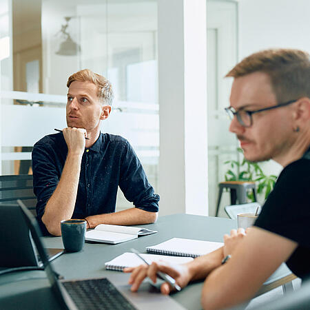 Zwei Mitarbeiter von visuellverstehen am Schreibtisch, die über eine Aufgabe nachdenken.