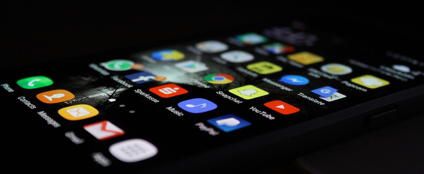 Ein leuchtendes Smartphonedisplay mit bunten App-Icons im Dunkeln.