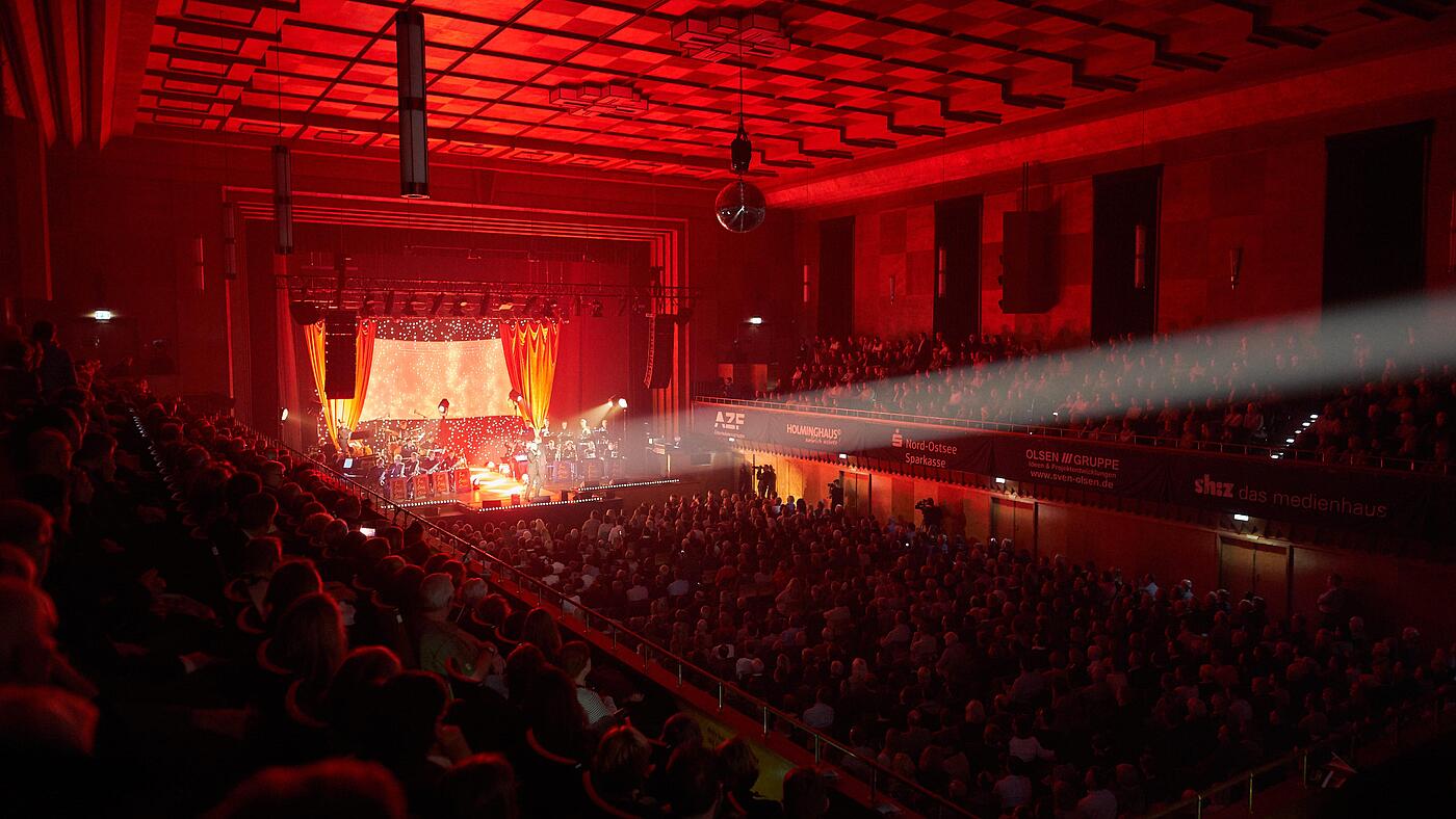 Person singt vor großem Publikum auf der Flensburg-singt-Sinatra-Veranstaltung, gehüllt in rotes Licht.