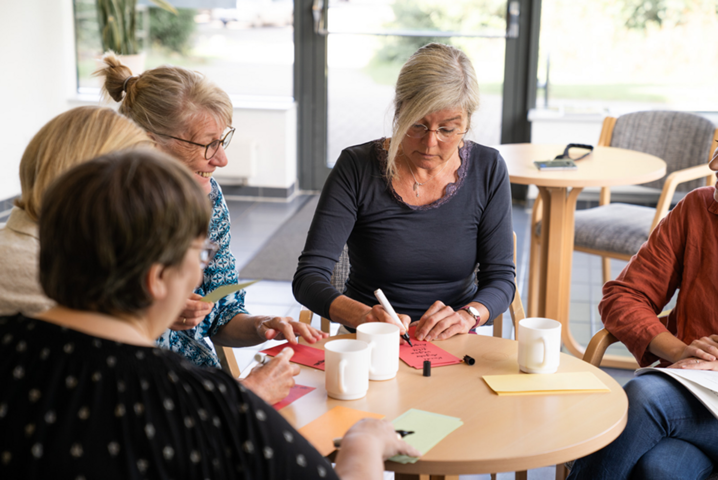 Teilnehmerinnen an einem der Workshops im VHS-Projekt sitzen am Tisch und schreiben auf bunte Moderationskärtchen.