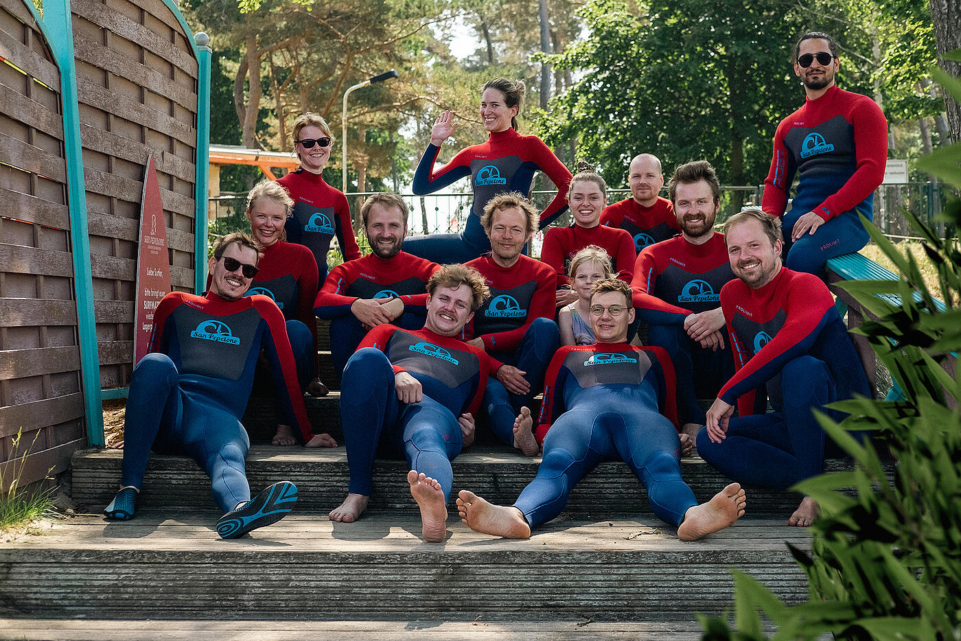 Das Team von visuellverstehen sitzt in Neoprenanzügen auf Holztreppen, rundherum grüne Vegetation.