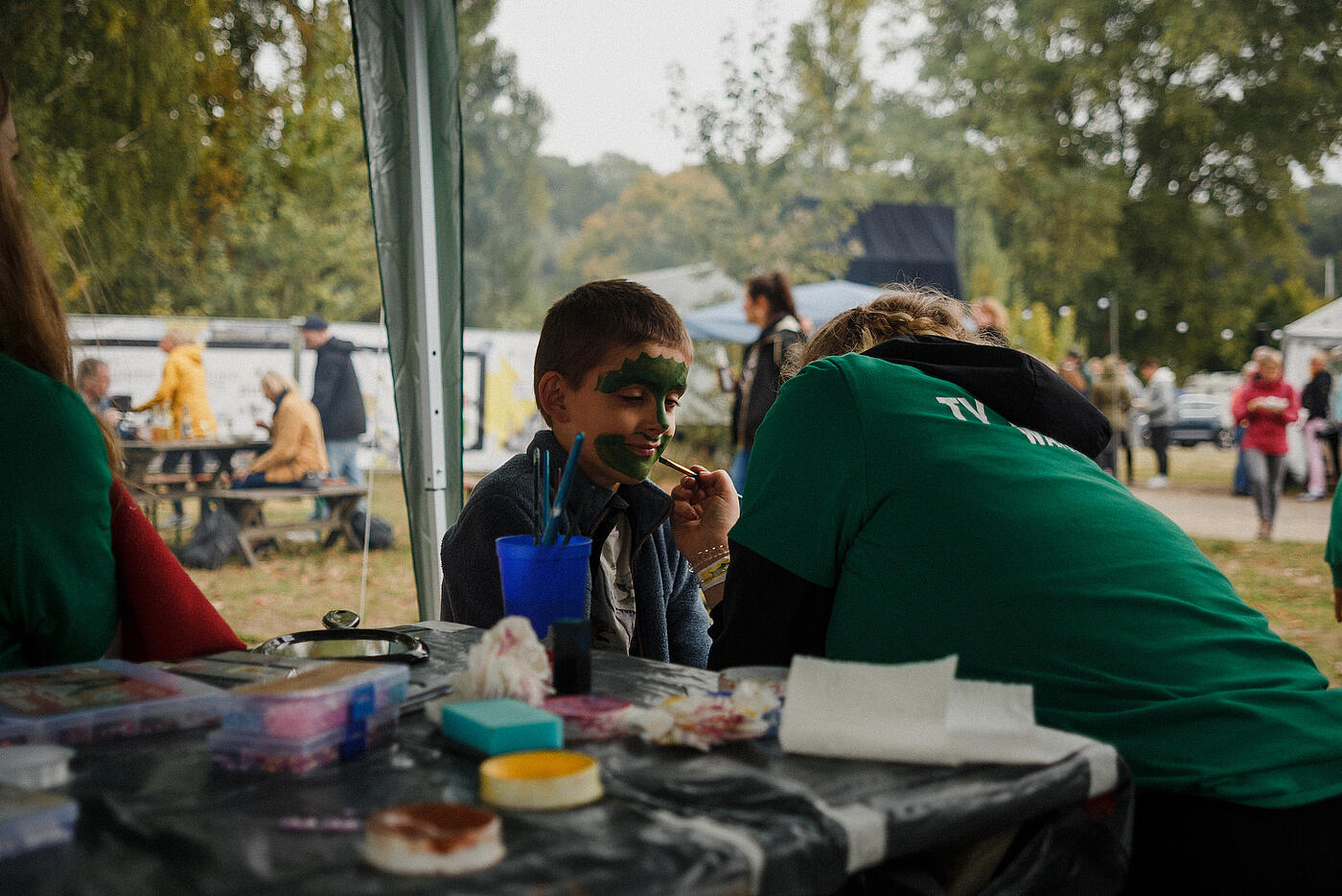 Einem kleinen Jungen wird das Gesicht grün geschminkt.