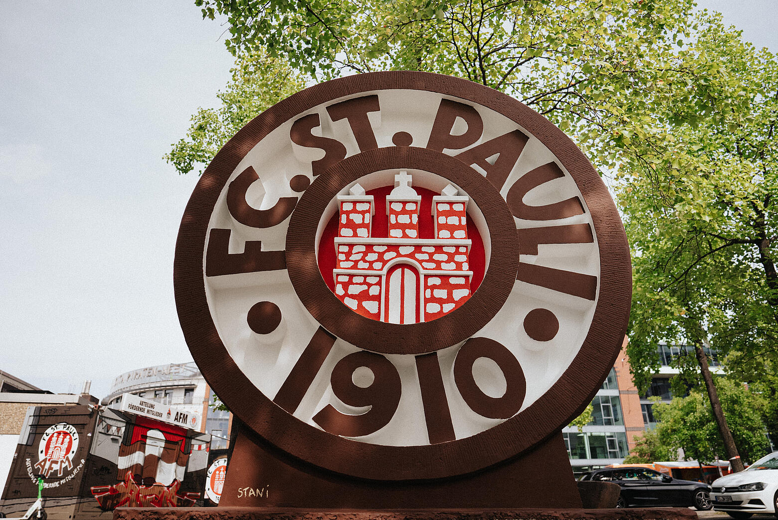 Betonskulptur des Wappens von FC St. Pauli auf einem von Bäumen umgebenen Platz, aus der Nähe fotografiert.