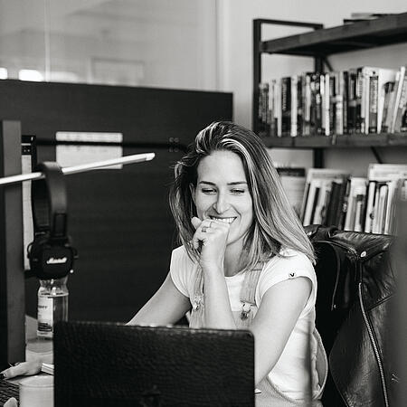 Eine Mitarbeiterin der Agentur visuellverstehen sitzt an ihrem Schreibtisch und schaut auf einen Laptop.