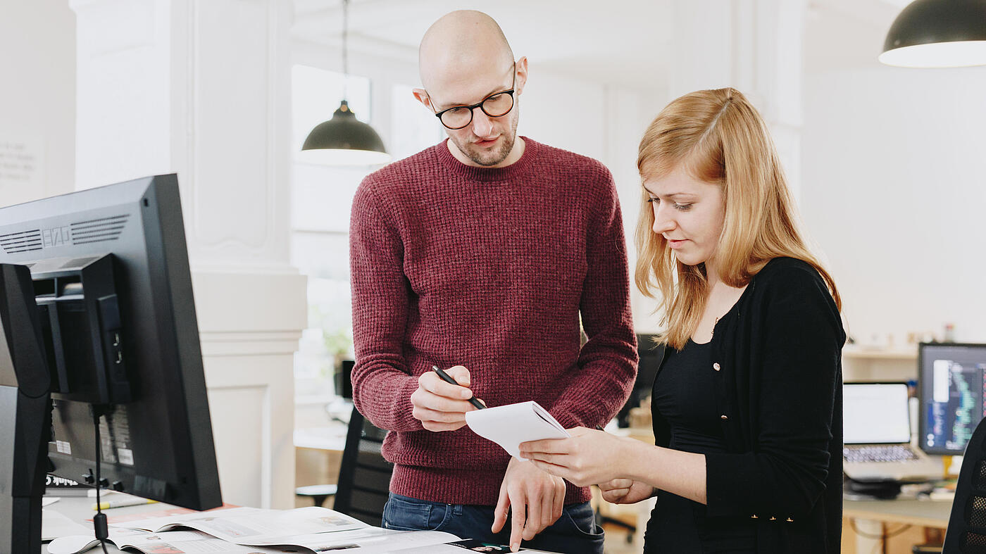 Zwei Personen aus dem Team von visuellverstehen stehen am Schreibtisch.