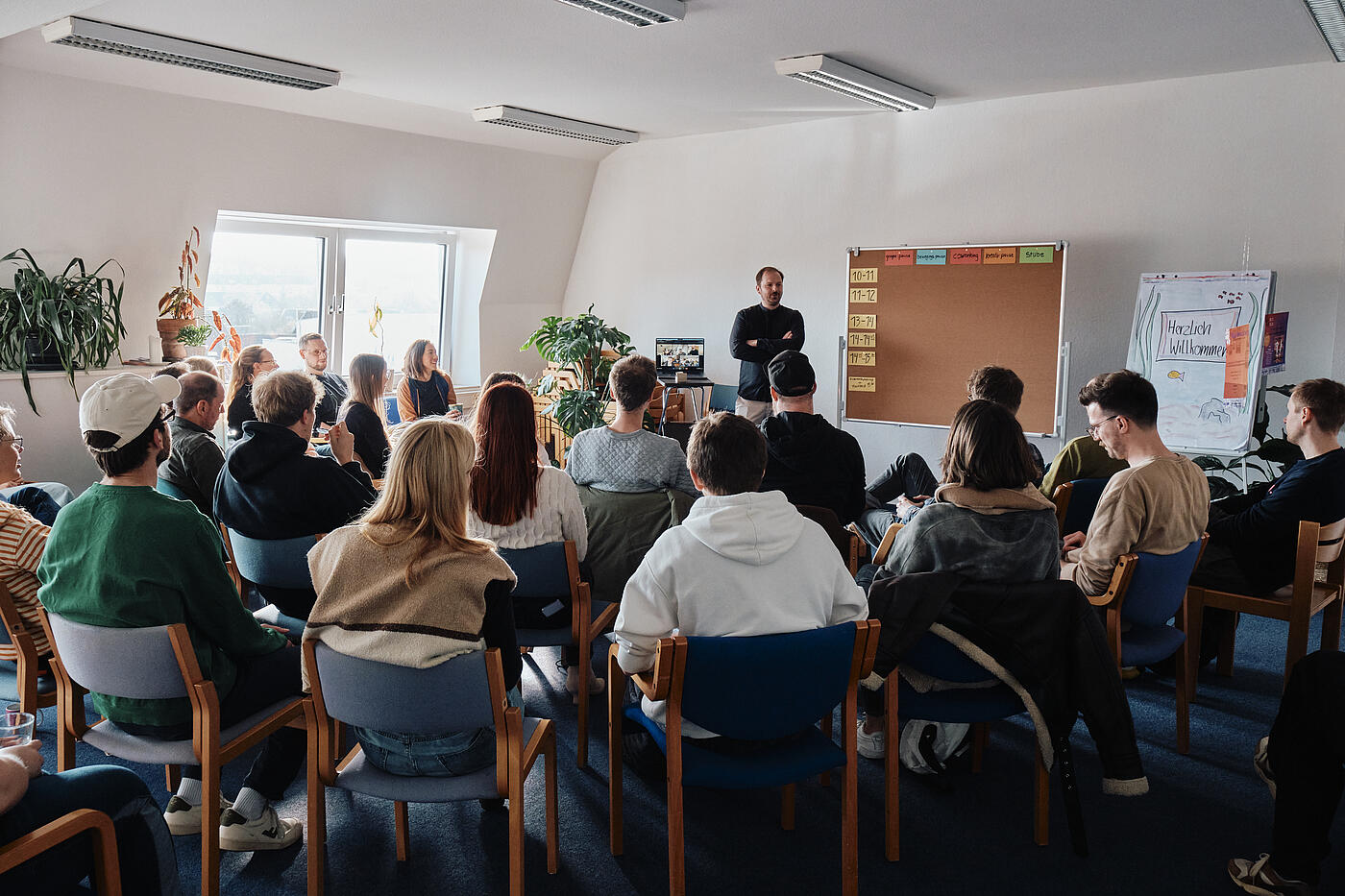 Blick von hinten auf das in Stuhlreihen zusammensitzende Team, das aufmerksam nach vorne schaut.