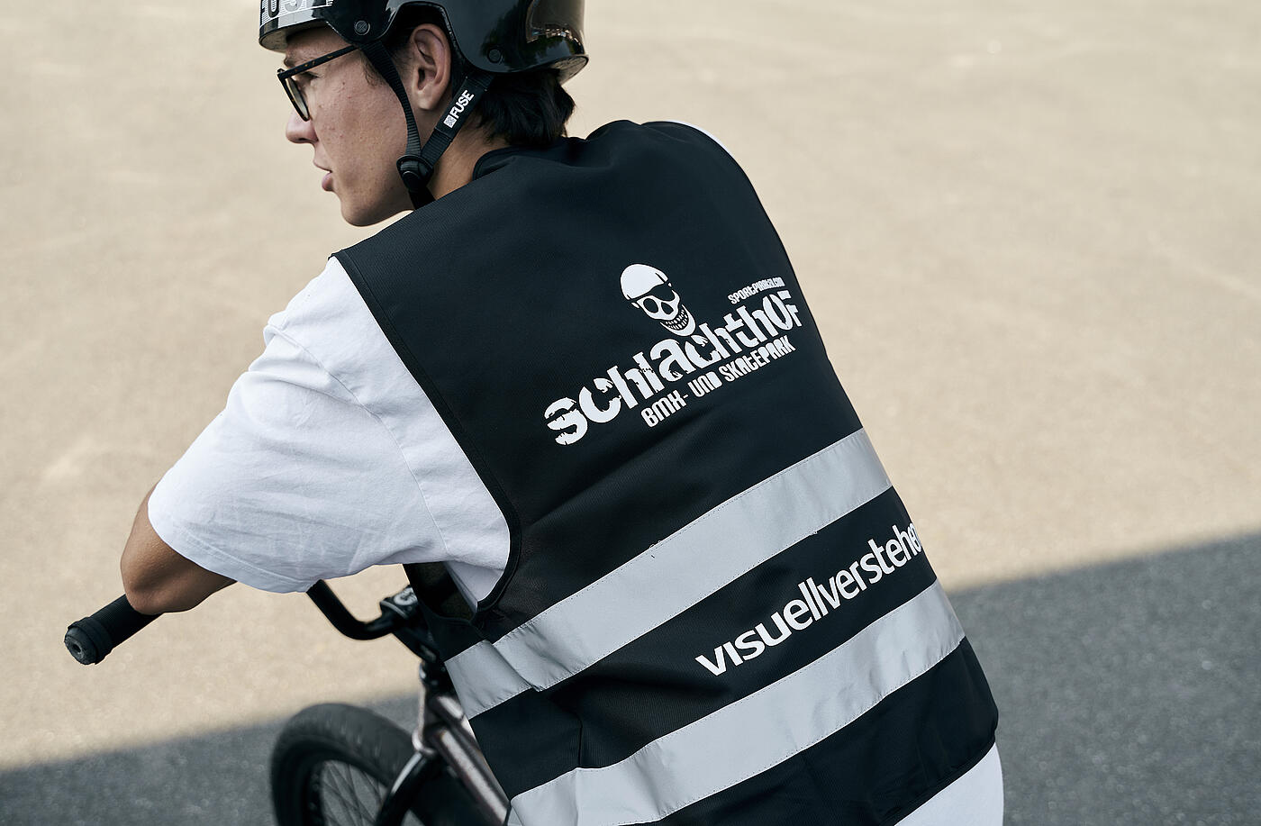 Ein junger BMX-Fahrer in der schwarzweißen Warnweste mit Sportpiraten- und visuellverstehen-Aufdruck auf seinem Rad.