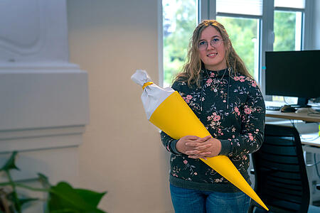 Eine Mitarbeiterin von visuellverstehen hält eine große gelbe Schultüte in der Hand.