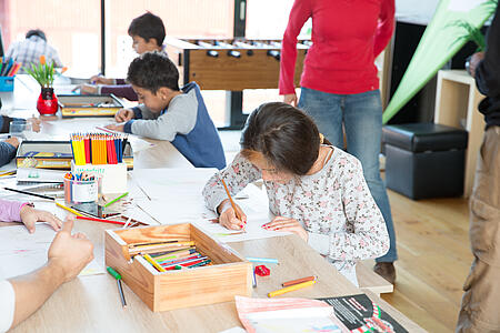 Kinder sitzen an einem Tisch voller bunter Malutensilien und malen.