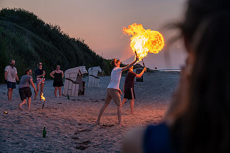 Mitarbeitende von visuellverstehen üben sich abends am Strand im Feuerspucken.
