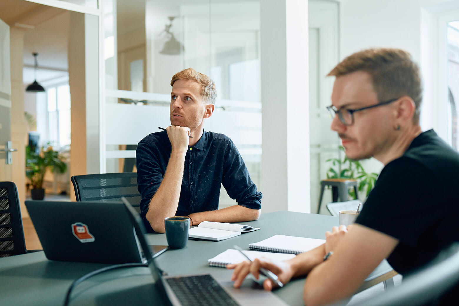 Zwei Mitarbeiter von visuellverstehen am Schreibtisch, die über eine Aufgabe nachdenken.