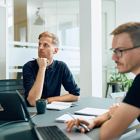 Zwei Mitarbeiter von visuellverstehen am Schreibtisch, die über eine Aufgabe nachdenken.