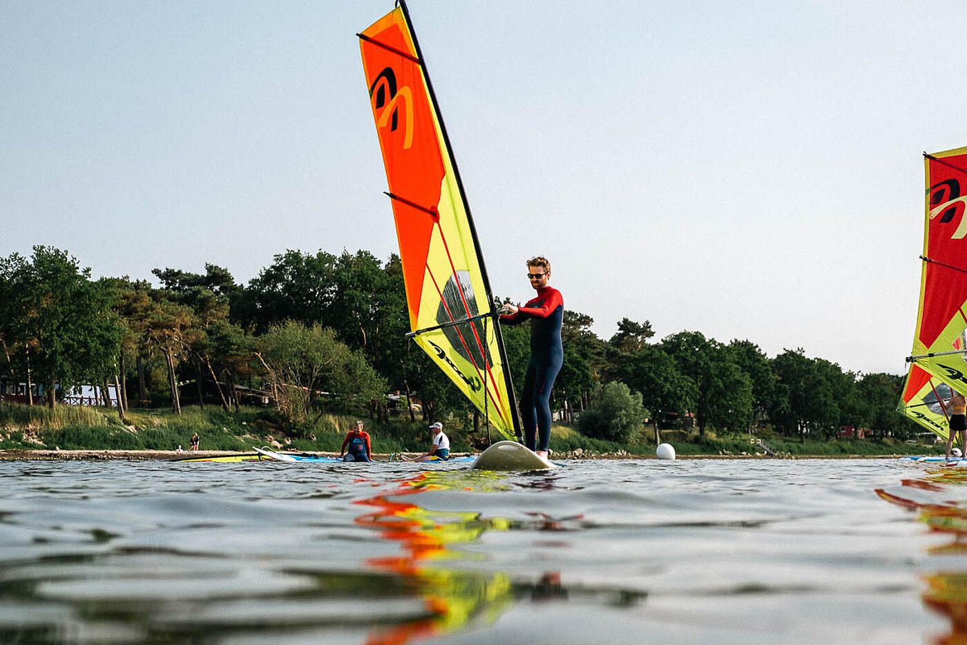 Ein Mitarbeiter von visuellverstehen lenkt sein Surfboard, im Hintergrund ein bewaldetes Ufer.