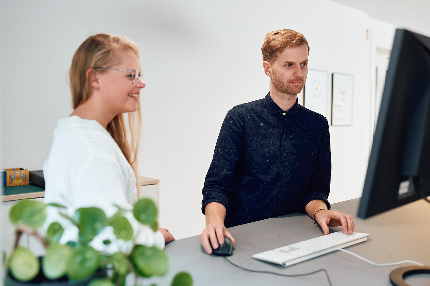 Vom Design zur Entwicklung: Zwei Mitarbeitende von visuellverstehen vor dem PC, im Vordergrund eine Pflanze..