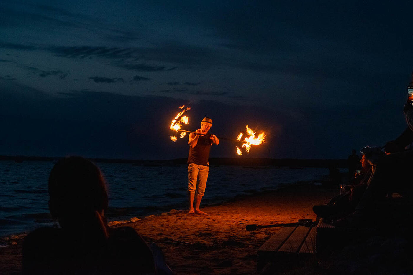 Eine Person führt am dunklen Strand eine Feuershow vor. 