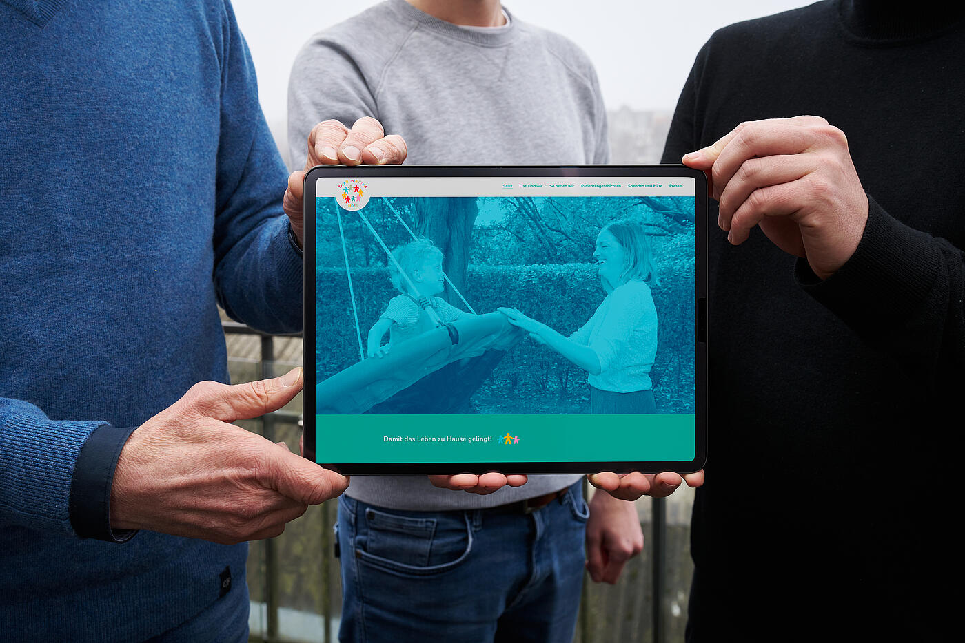 Mehrere Hände halten ein Tablet in die Kamera, auf dem die von visuellverstehen geschaffene Website zu sehen ist.