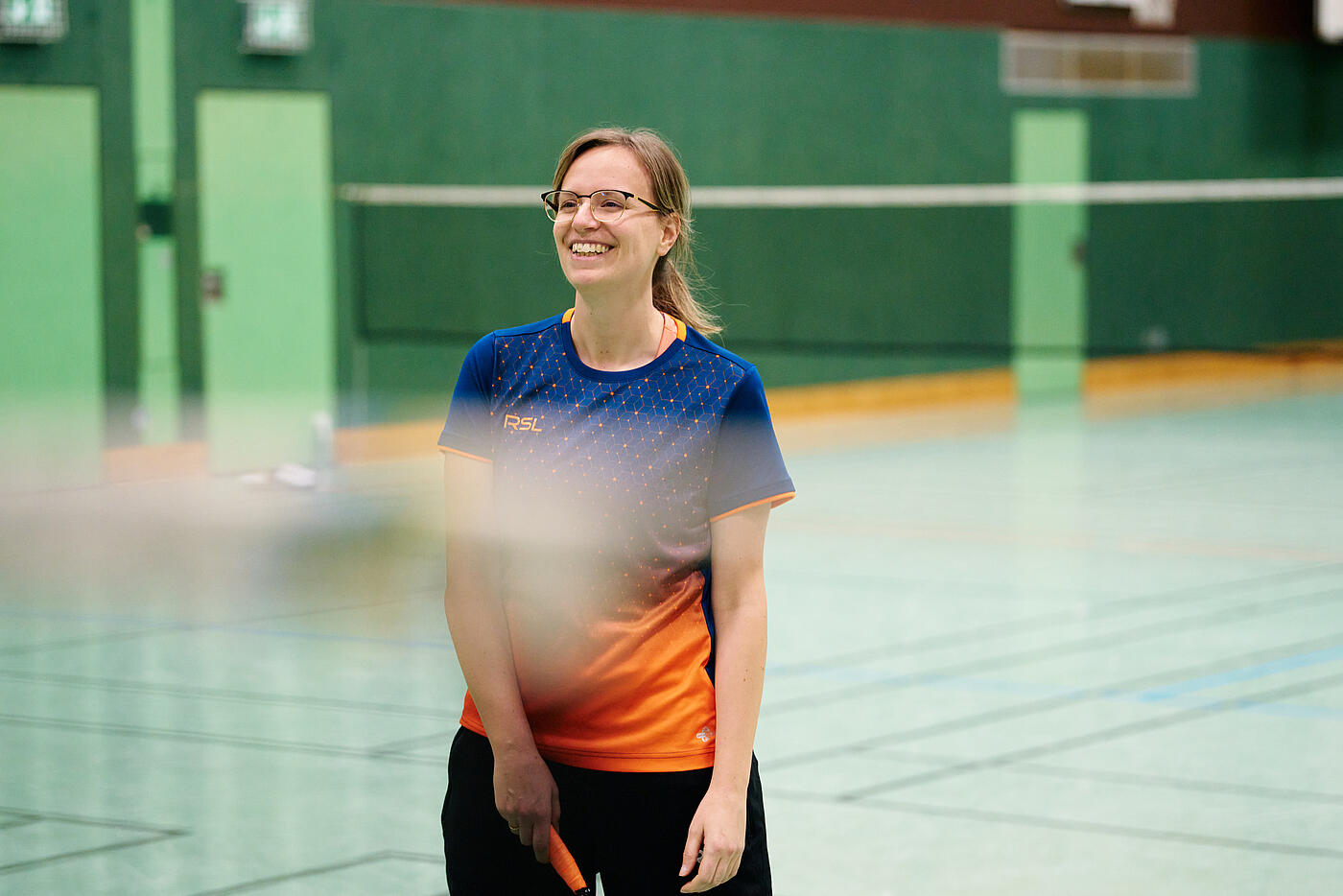 Eine Mitarbeiterin von visuellverstehen spielt Badminton in einer Turnhalle.