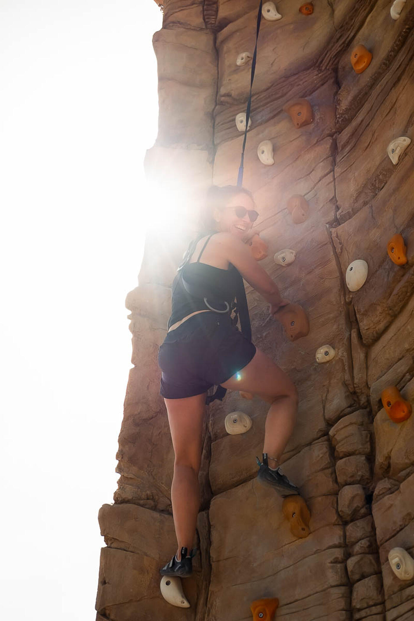 Eine Mitarbeiterin von visuellverstehen klettert lachend eine Boulderwand hinauf.