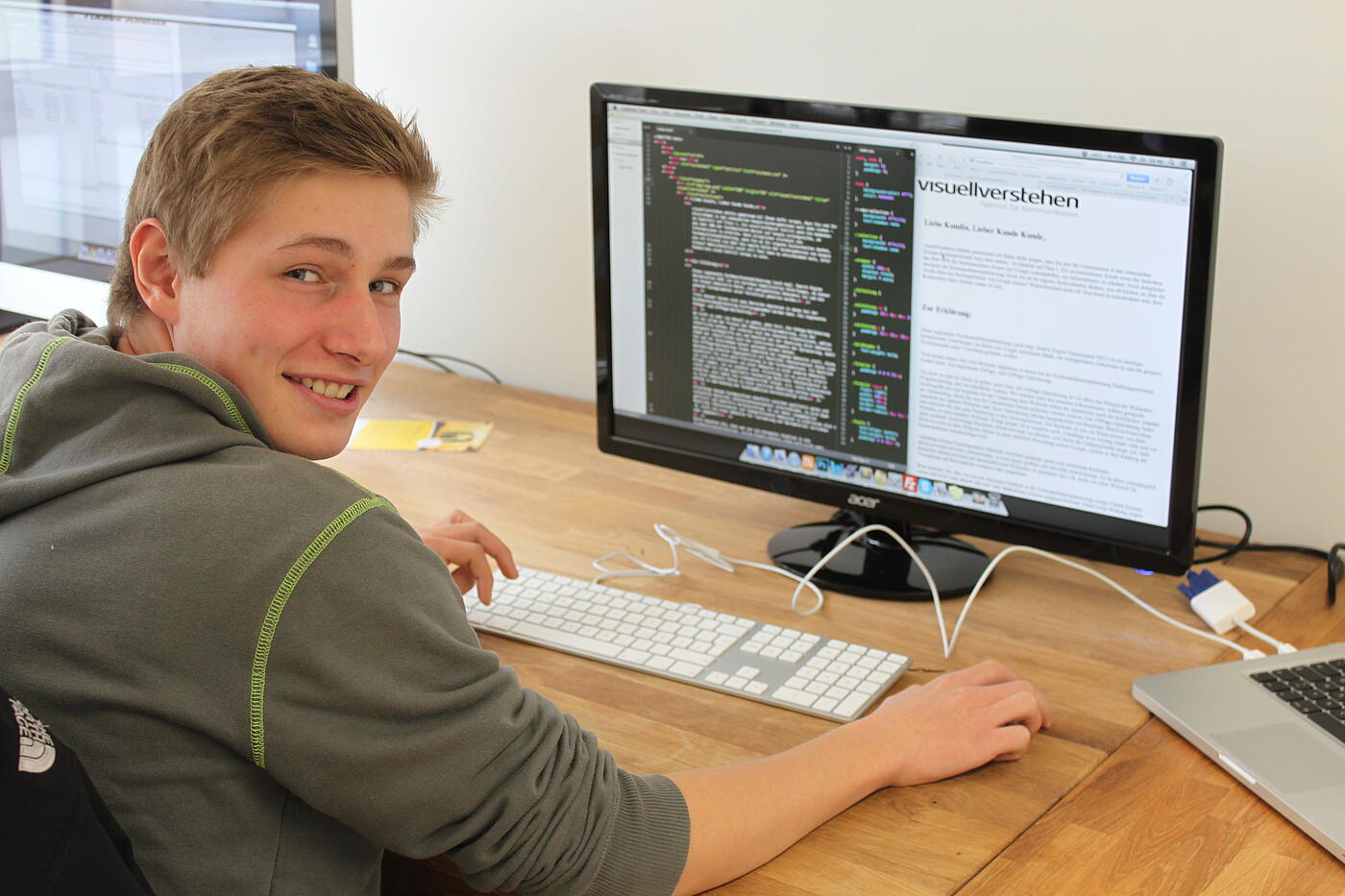 Rune sitzt an einem Schreibtisch mit Computer. Lächelnd blickt er über seine rechte Schulter.
