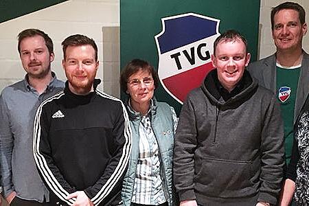 Gruppenfoto: Der Vorstand des TV Grundhof vor dem Wappen des Sportvereins in einem Innenraum.