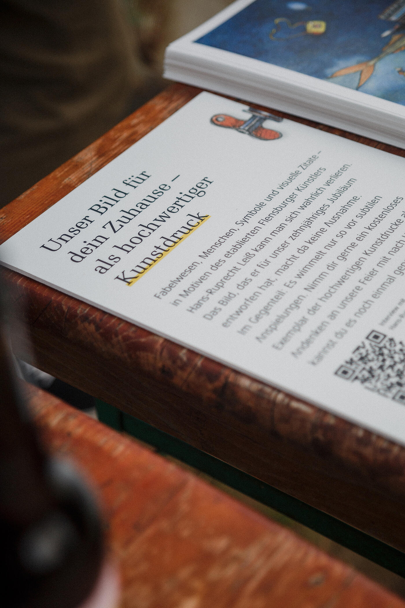 Der Bildausschnitt zeigt eine Informationskarte, auf der Besucher*innen des Jubiläumsfests lesen können, dass sie sich Kunstdrucke des norddeutschen Künstlers Leiß kostenlos mitnehmen dürfen.