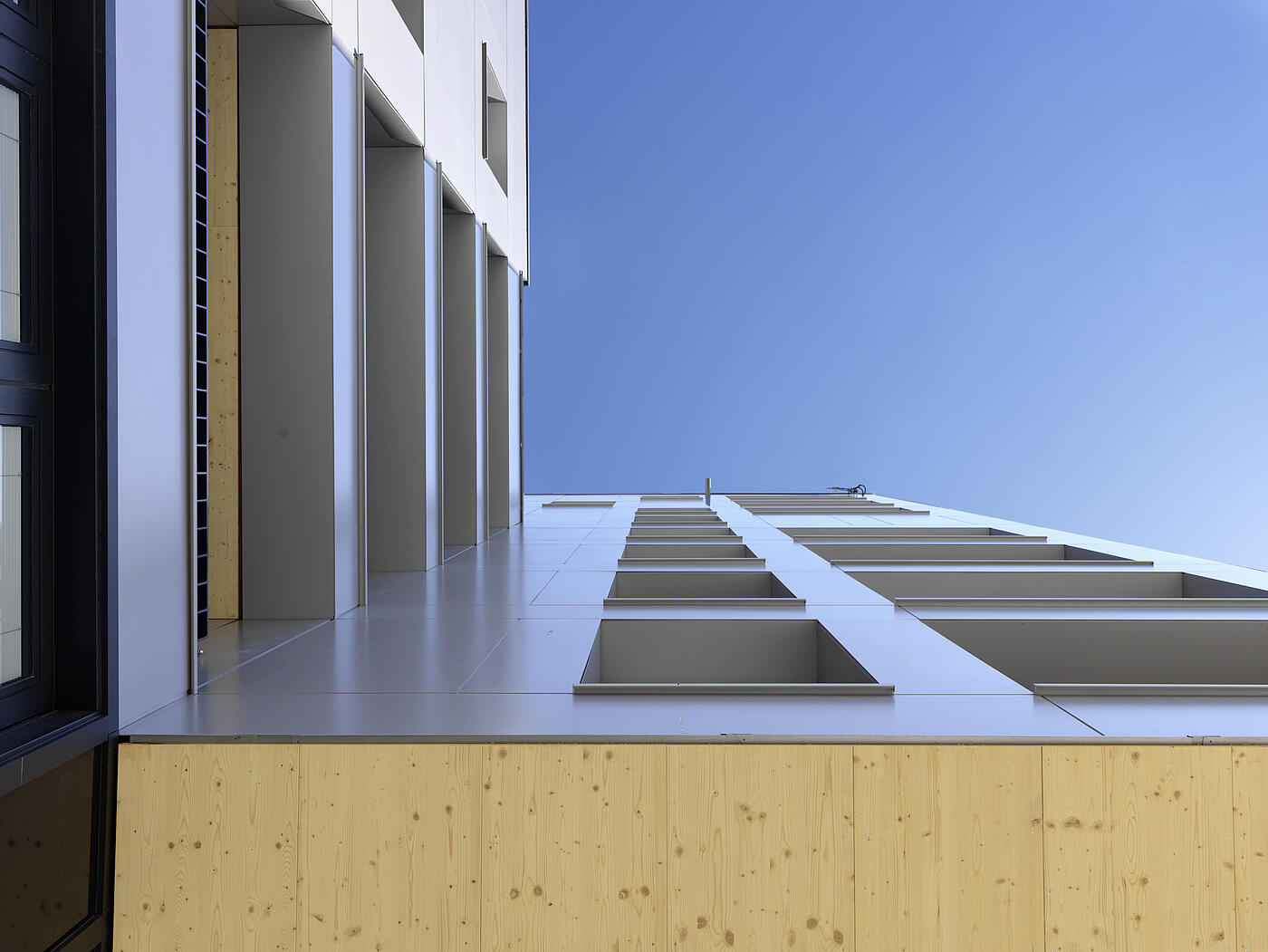 Ein Gebäudeausschnitt mit klaren Linien und Holzanteilen vor blauem Himmel.