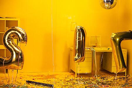 Ausschnitt aus dem vv-Film 2017: Goldene Zahlen-Luftballons schweben in einem gelb gestrichenen Raum.
