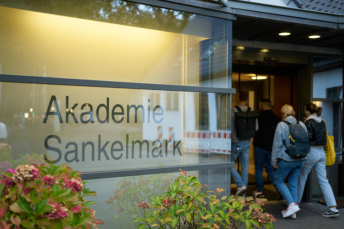 Junge Menschen mit Rucksäcken betreten einen Eingang. An der Scheibe steht Akademie Sankelmark.
