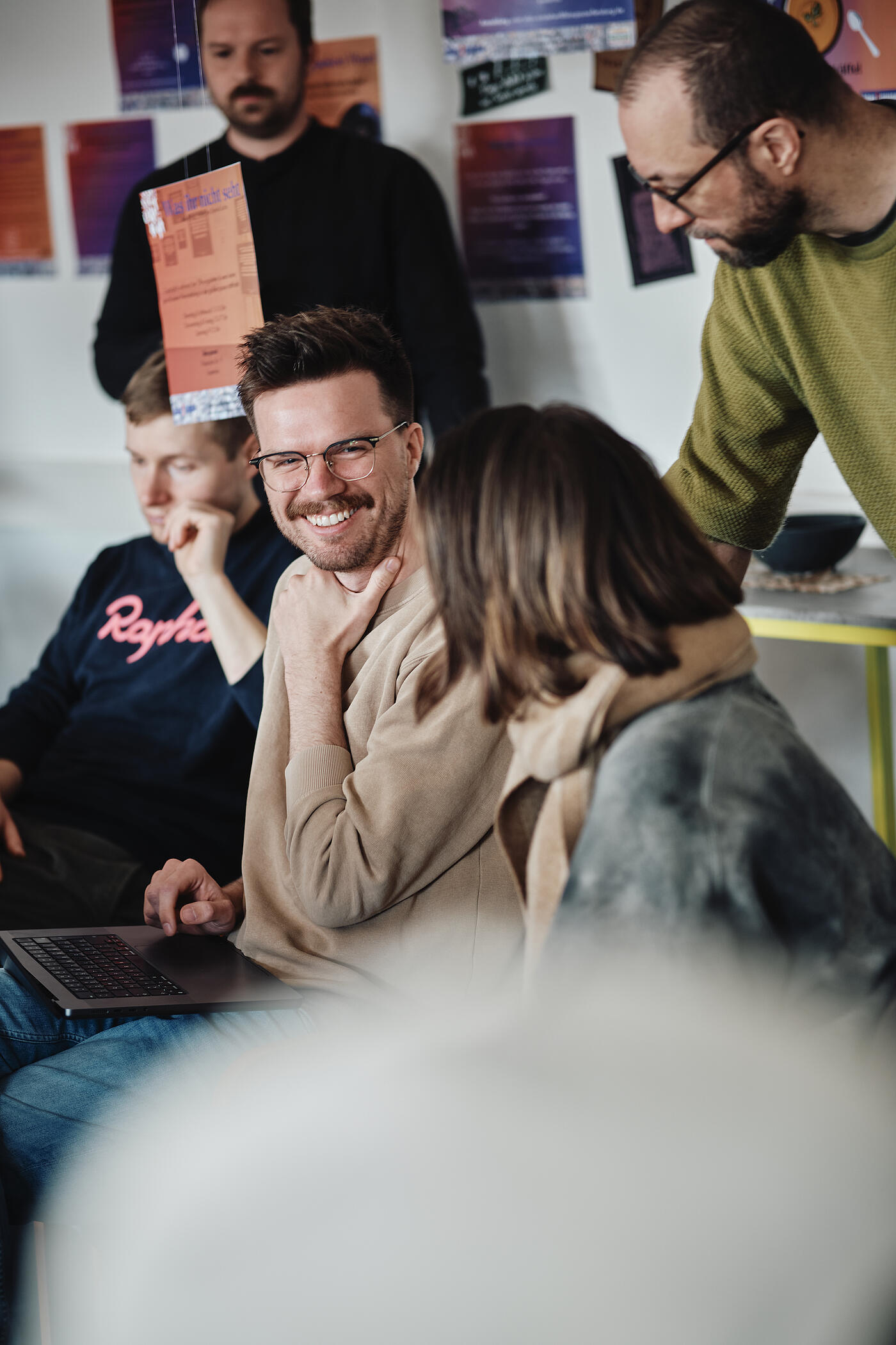 Ein Mann mit einem Laptop auf dem Schoß schaut zu seiner Sitznachbarin und lacht.