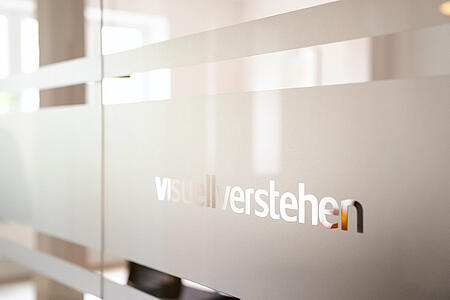 Der visuellverstehen-Schriftzug auf einer Glastür.