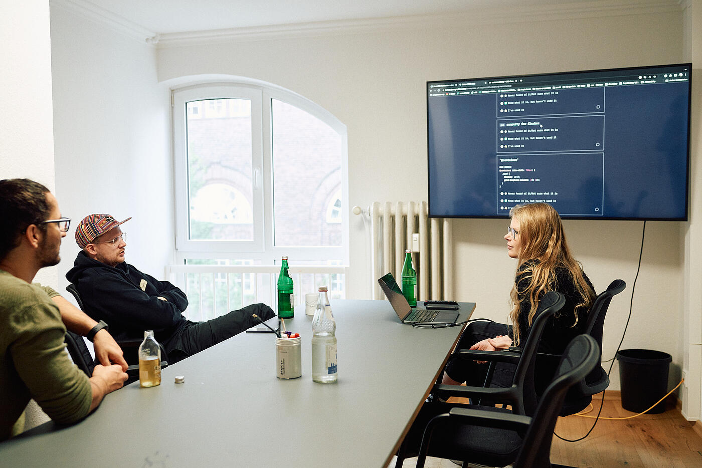 Drei Mitarbeitende aus der Entwicklung schauen auf einen Wandbildschirm mit Quellcode.
