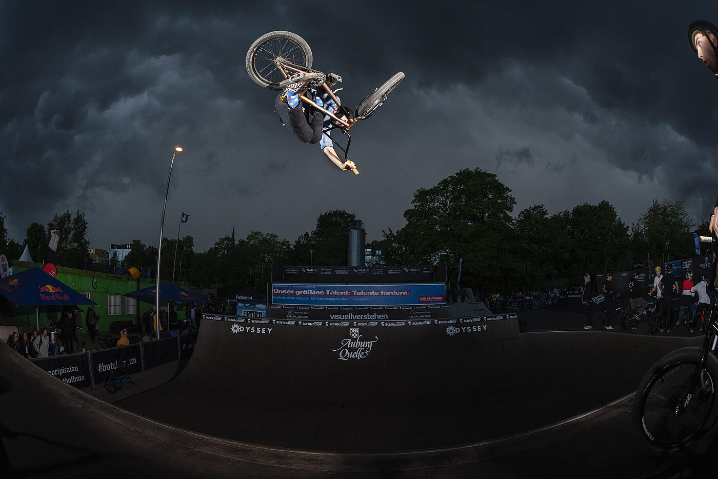 Ein BMX-Fahrer dreht sich nachts am oberen Rand einer Halfpipe in der Luft.