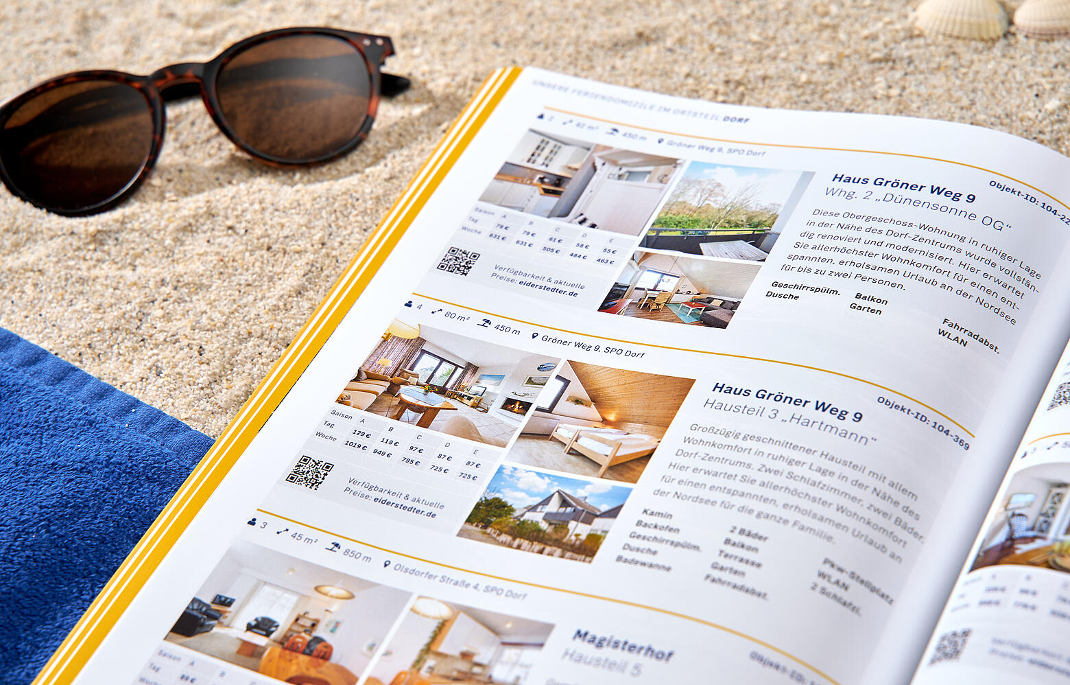 Eine aufgeschlagene Ausgabe des Eiderstedter-Magazins liegt am Strand zwischen einem Handtuch und einer Sonnenbrille.