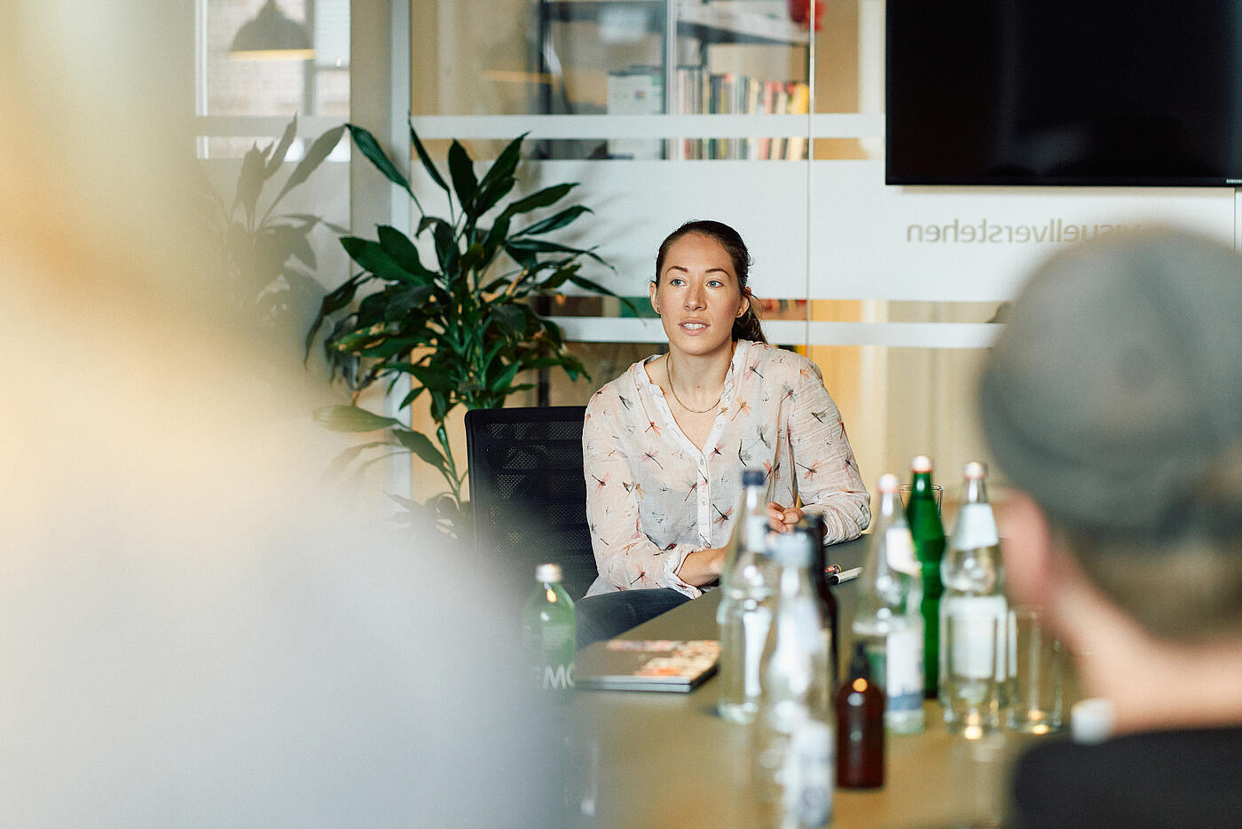 Eine Mitarbeiterin von visuellverstehen sitzt lächelnd im Besprechungsraum am Tisch.