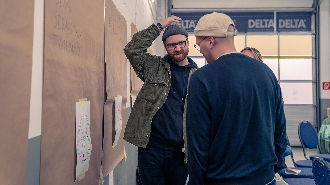 Drei Mitarbeiter von visuellverstehen stehen vor einer Wand, an die Packpapier geklebt ist, und besprechen etwas.