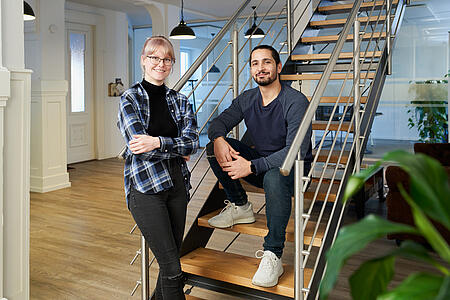 Zwei Mitarbeitende von visuellverstehen lehnen an der Treppe in den modernen Büroräumen der Agentur.