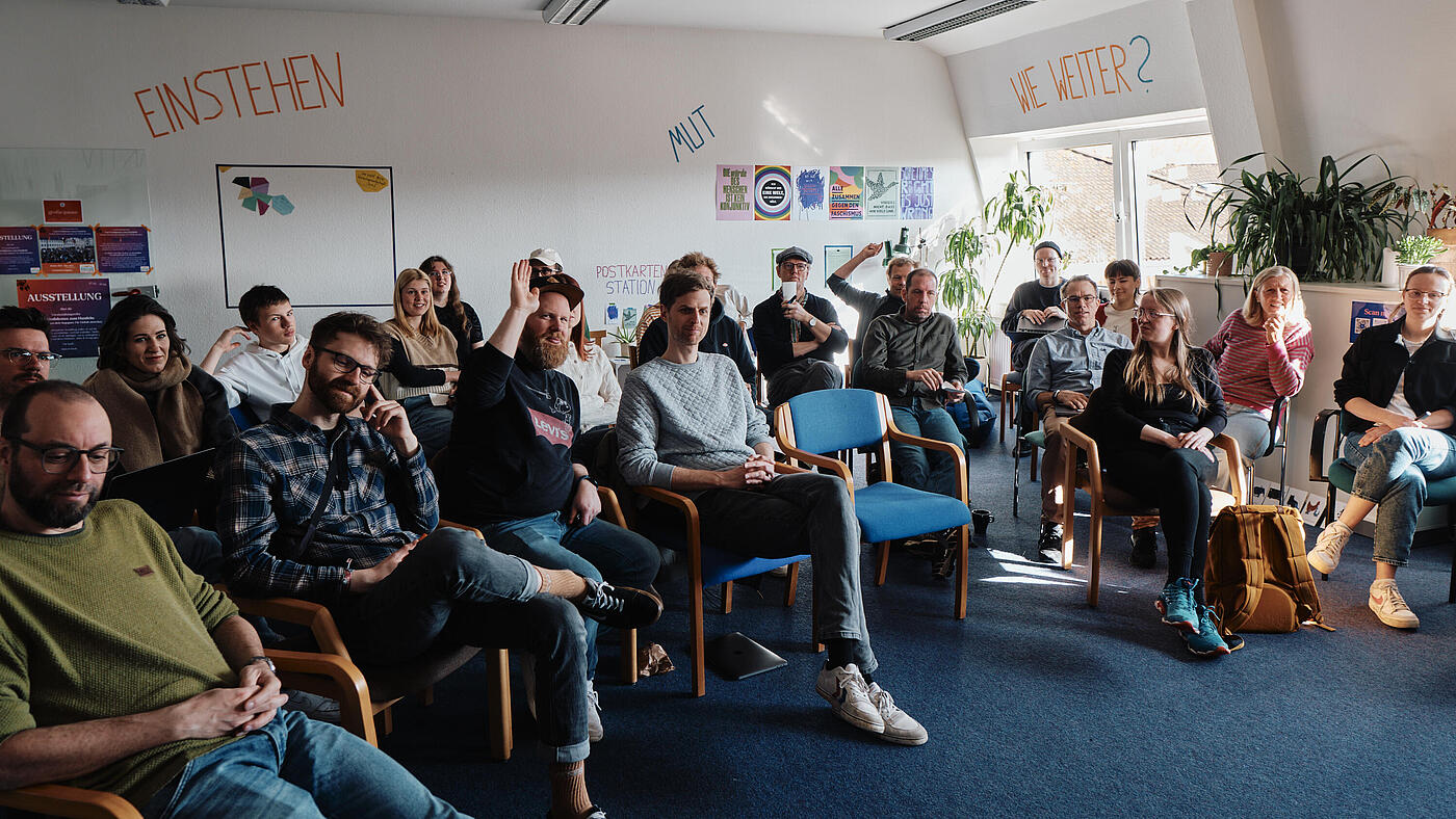 Das Team sitzt in Stuhlreihen zusammen und blickt nach vorne.