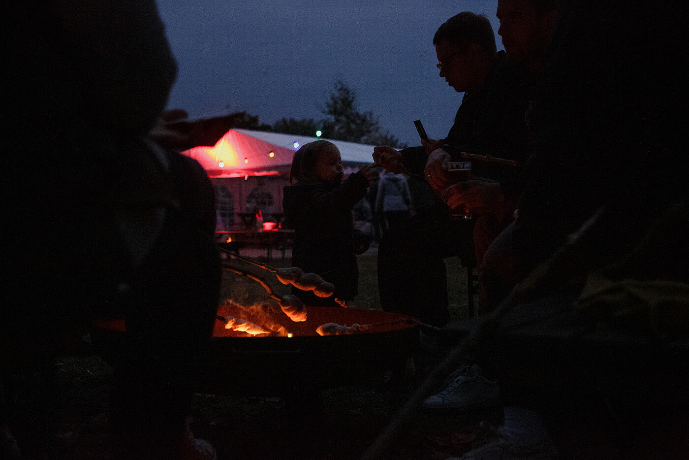 Ein Lagerfeuer glimmt im Dunkeln, darüber wird Stockbrot gebacken.