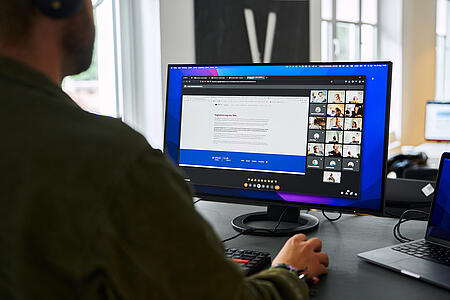 Schulterblick bei einem Mitarbeiter von visuellverstehen vor dem Bildschirm, auf dem eine Videokonferenz läuft.