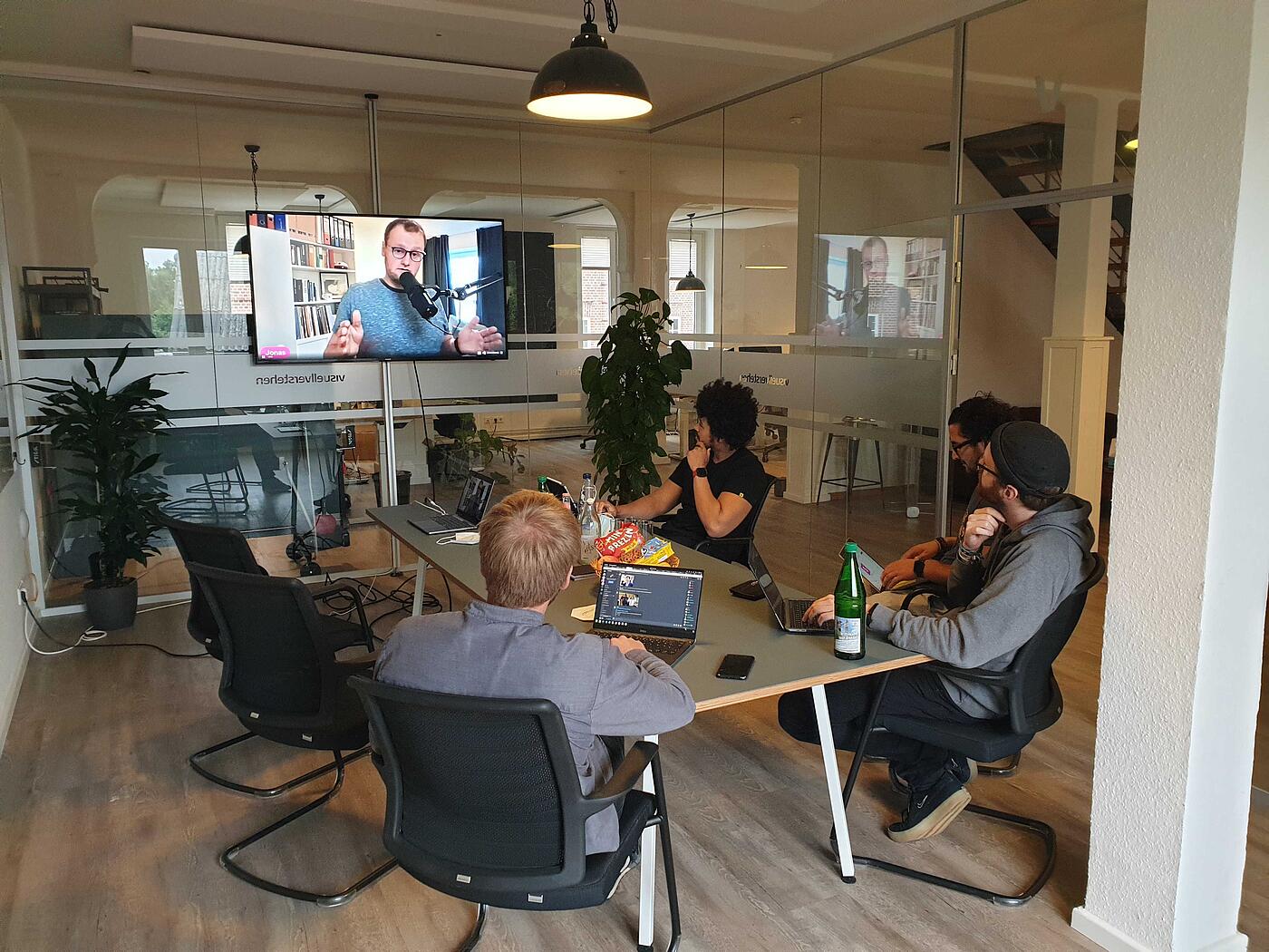 Mehrere Mitarbeiter von visuellverstehen sitzen in einem modernen Besprechungsraum und schauen auf einen Bildschirm an der Wand.