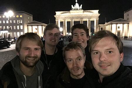 Mehrere Mitarbeiter von visuellverstehen stehen vor dem Brandenburger Tor und schauen in die Kamera. Es ist Nacht.