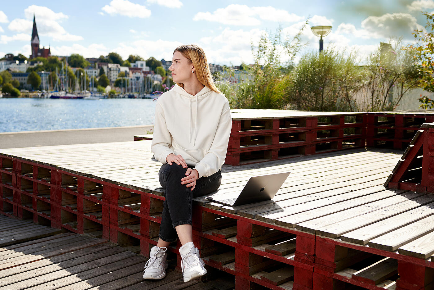 Eine Mitarbeiterin von visuellverstehen sitzt am Flensburger Hafen in der Sonne und blickt über die Schulter..