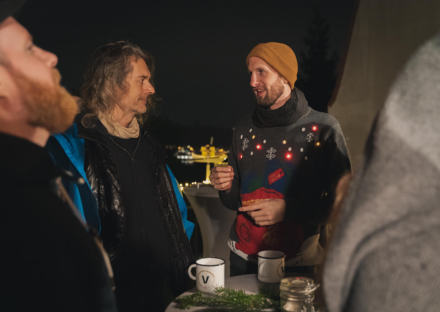 Mitarbeitende und Kund*innen von visuellverstehen beim Punschen auf der Dachterrasse des Unternehmens, im Zentrum ein Mitarbeiter in auffälligem Weihnachtspulli..