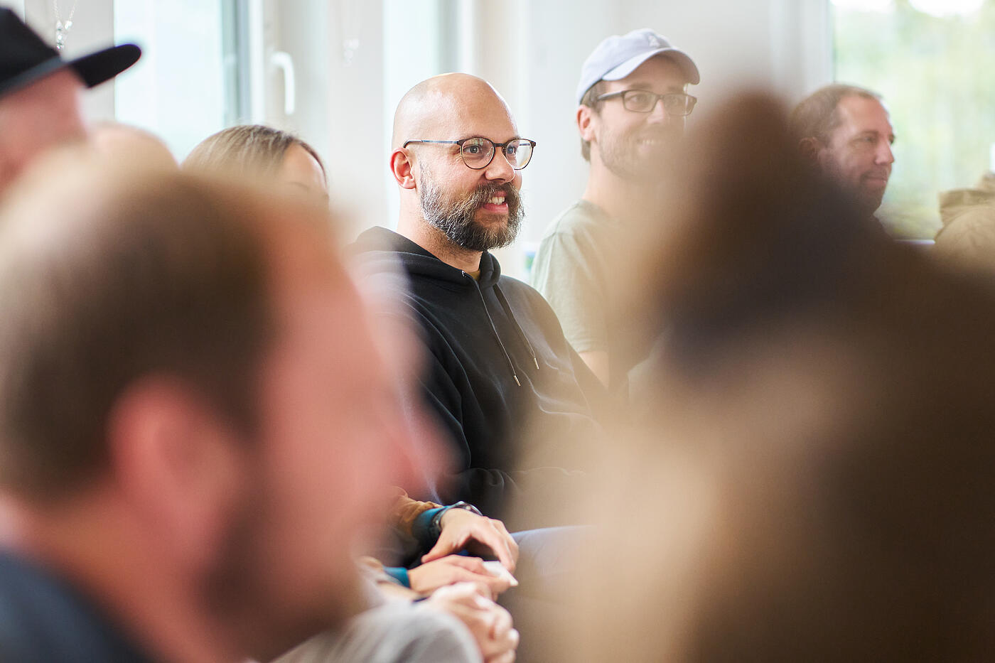 Lachender Mann mit Vollbart, Brille und Glatze im schwarzen Hoodie.