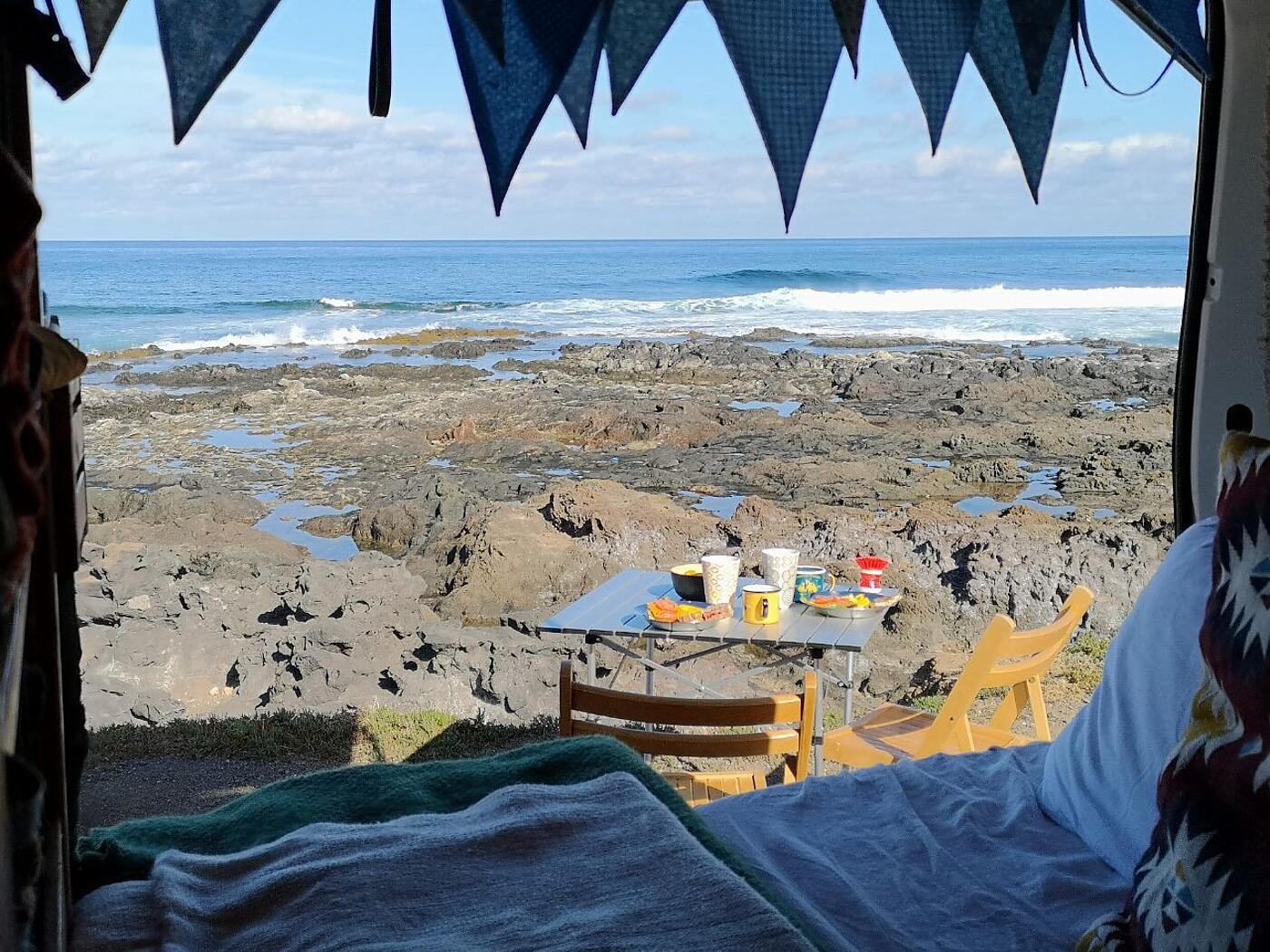 Der Blick aus dem Inneren des VW-Busses hinaus, dahinter Strand und blauer Himmel.