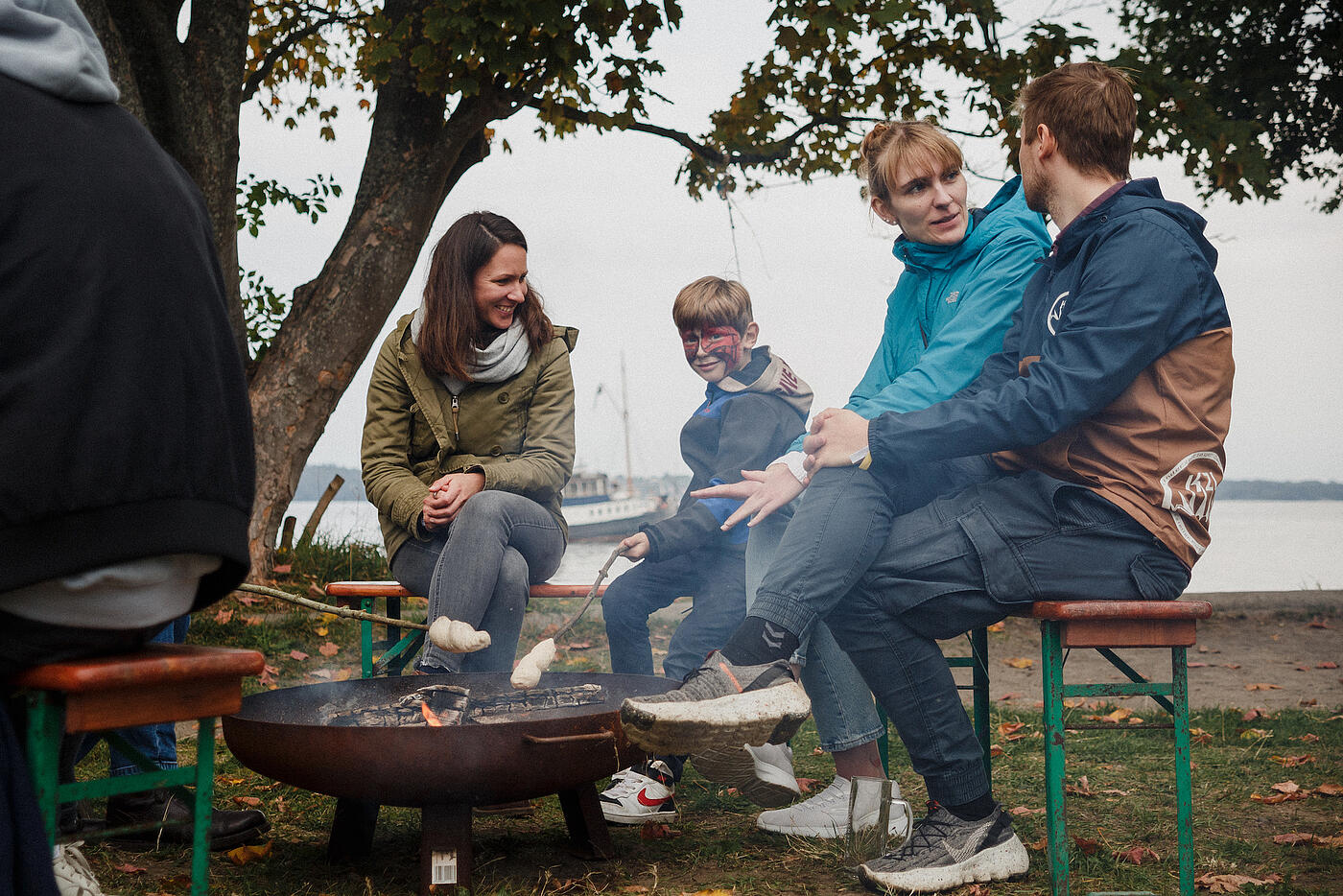 Mitarbeitende und ihre Familien sitzen am Feuer und rösten Stockbrot.