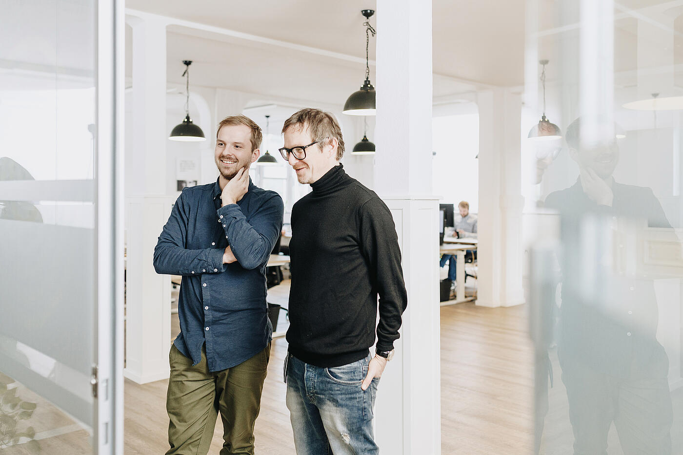 Zwei Mitarbeiter von visuellverstehen stehen vor der Tür des verglasten Besprechungsraums.