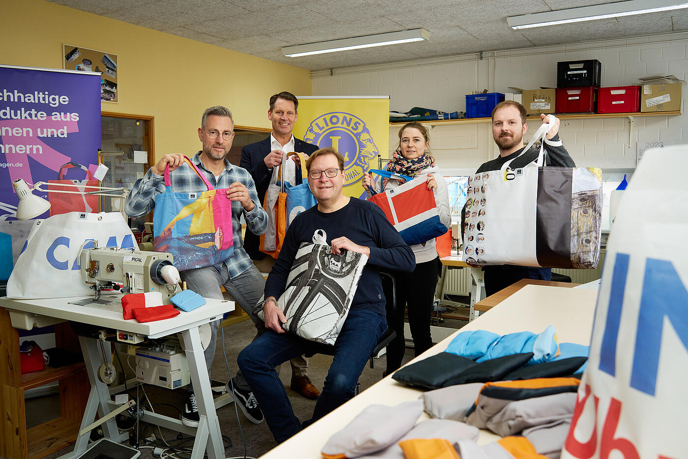 Mehrere Personen posieren in einem Nähstudio und halten bunte Beutel in die Kamera.