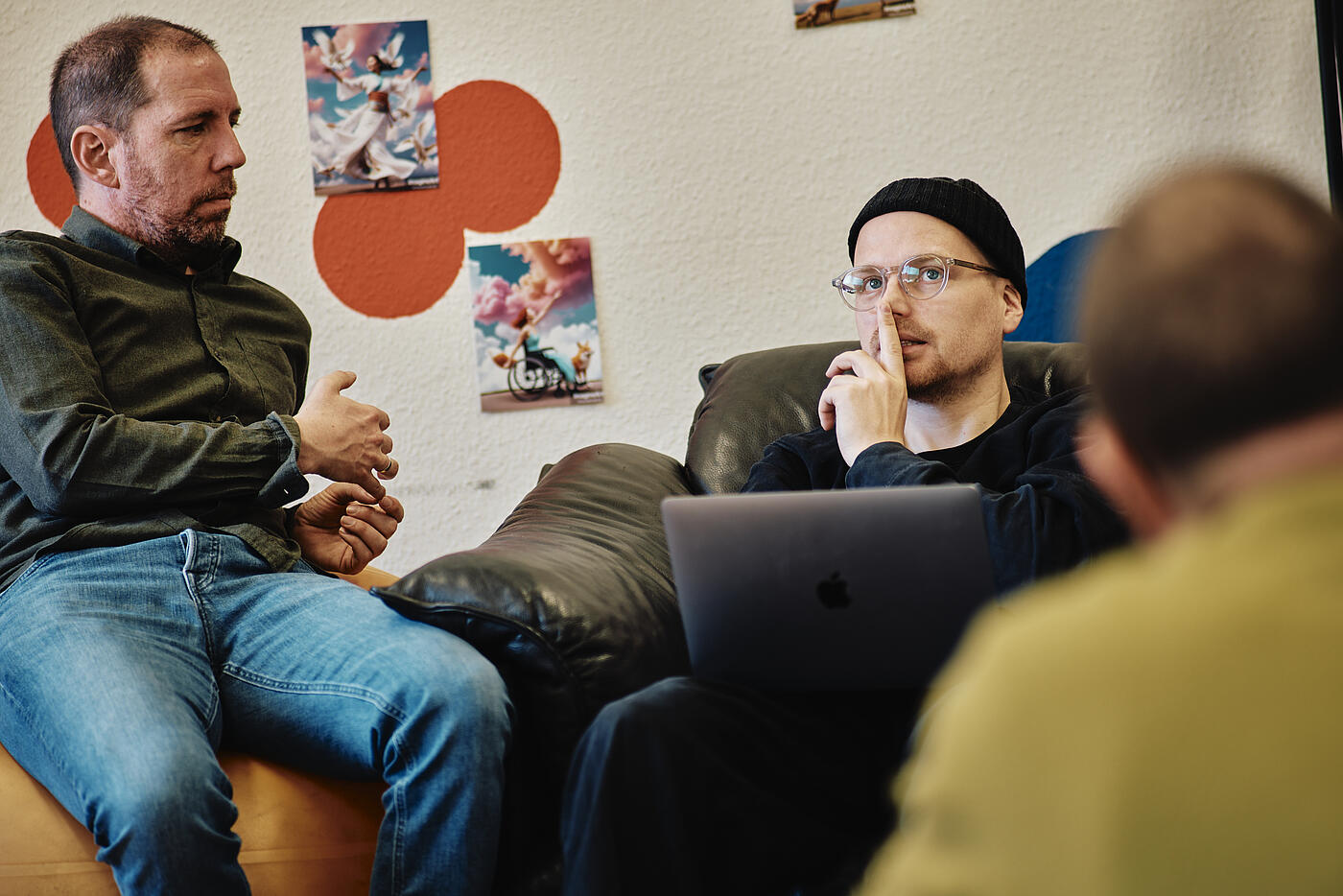 Drei Mitarbeiter von visuellverstehen sitzen auf verschiedenen Sitzgelegenheiten zusammen und unterhalten sich.