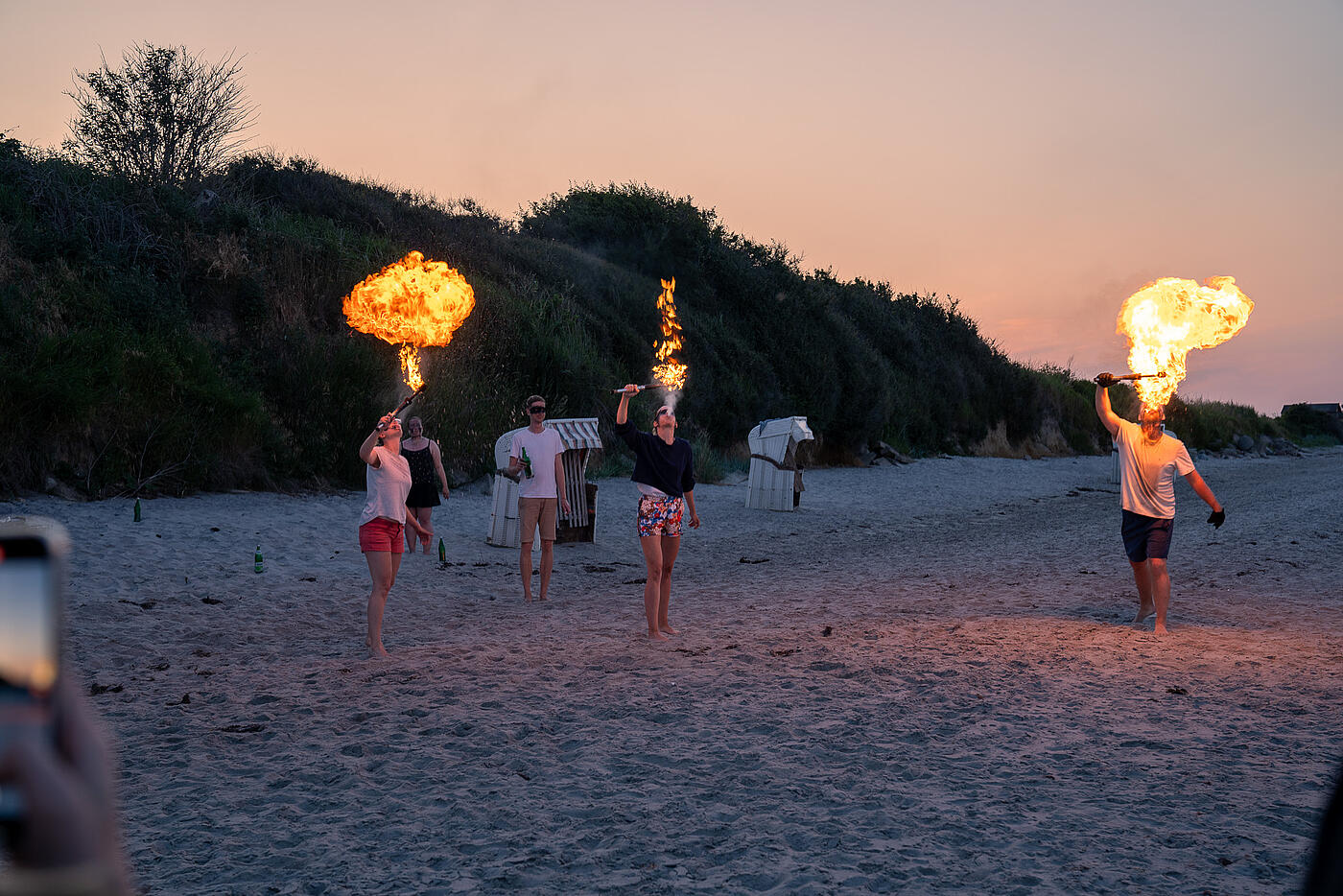 Mitarbeitende von visuellverstehen üben sich abends am Strand im Feuerspucken.